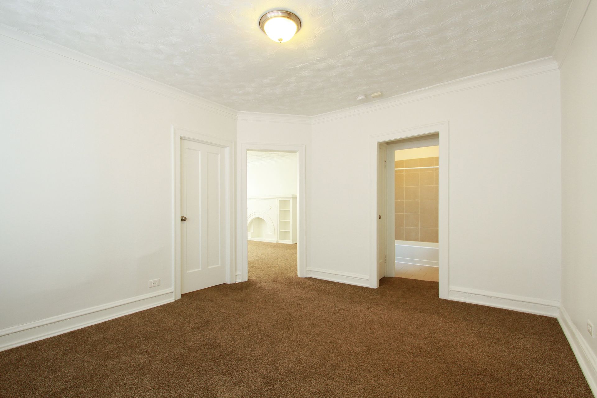 Empty room with brown carpet, white walls, and three doorways.