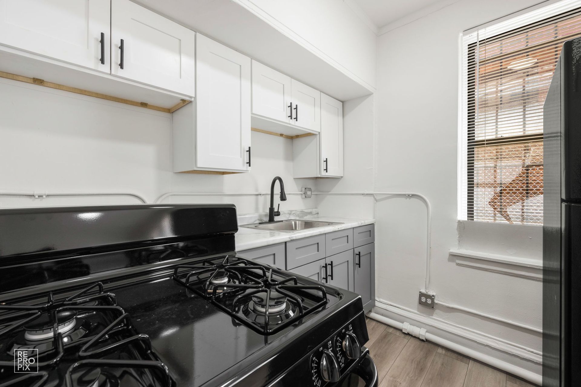 Kitchen with gray and white cabinets, black stove, and a window with blinds.