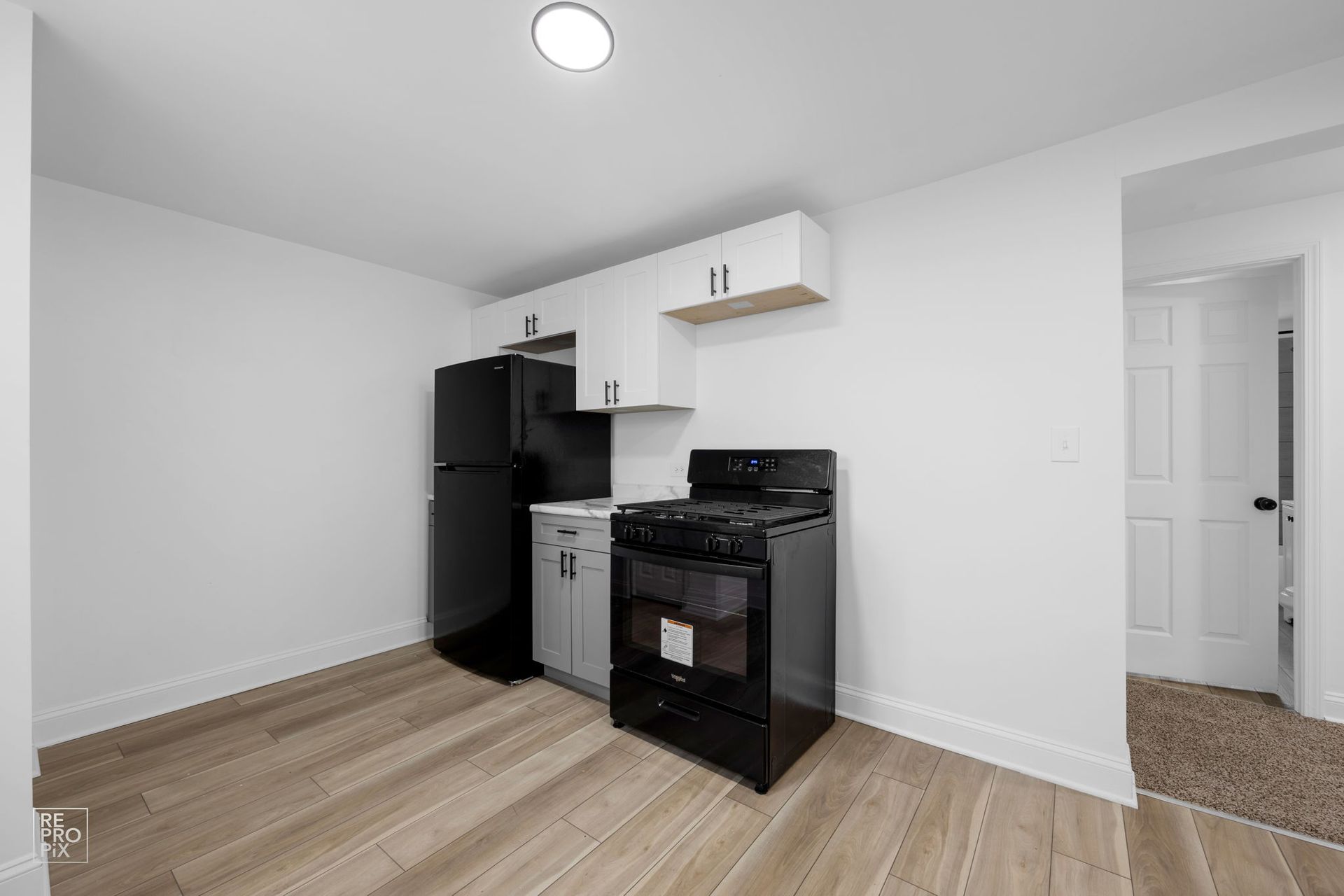 Small kitchen with black appliances, white cabinets, and wood-look flooring. A door is visible on the right.