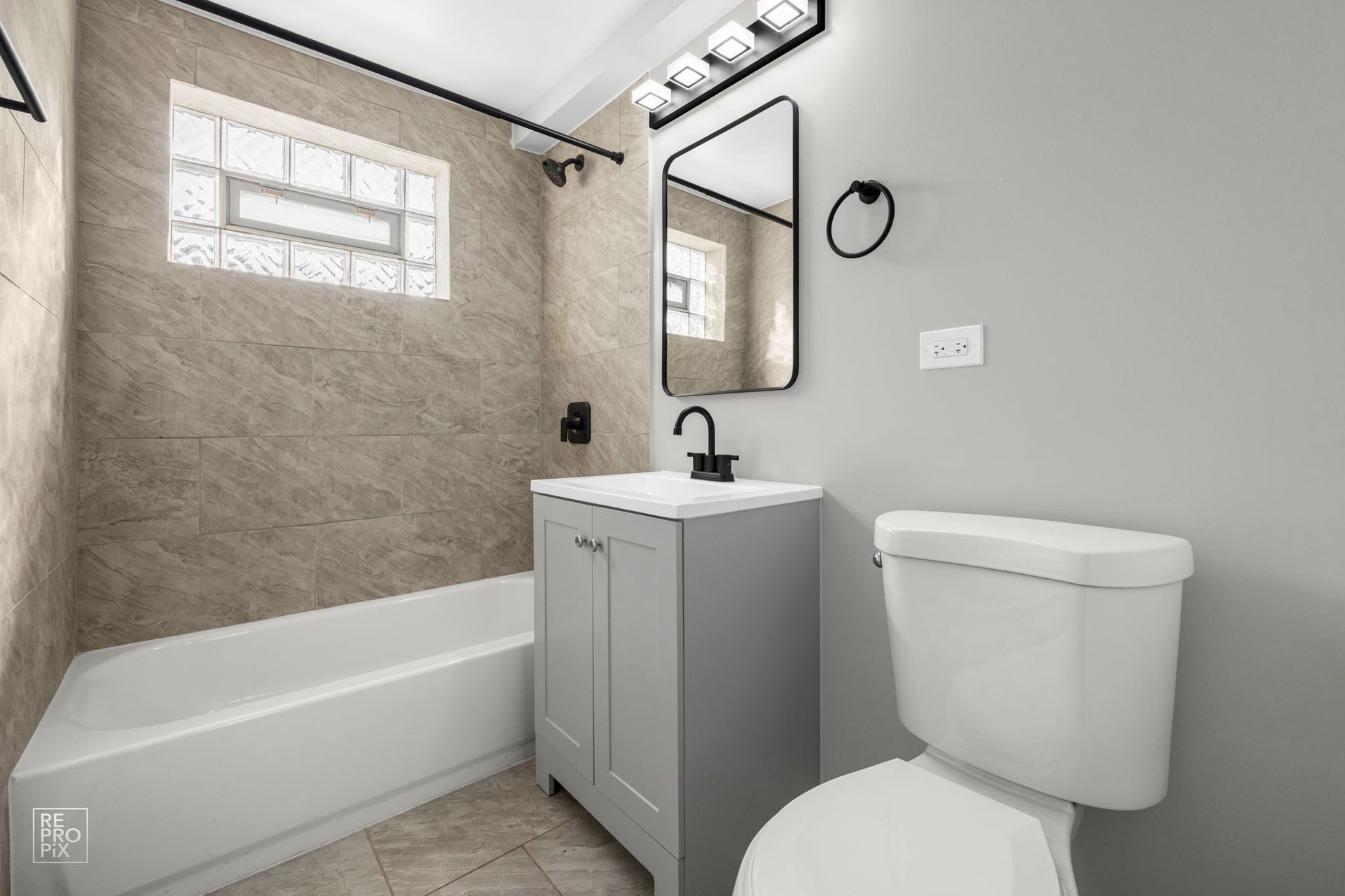 Bathroom with gray walls, white bathtub and toilet, and gray vanity with a black faucet.