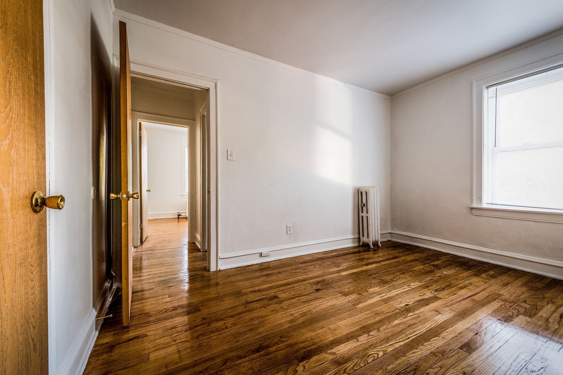 Empty room with wooden floors, white walls, and a window.