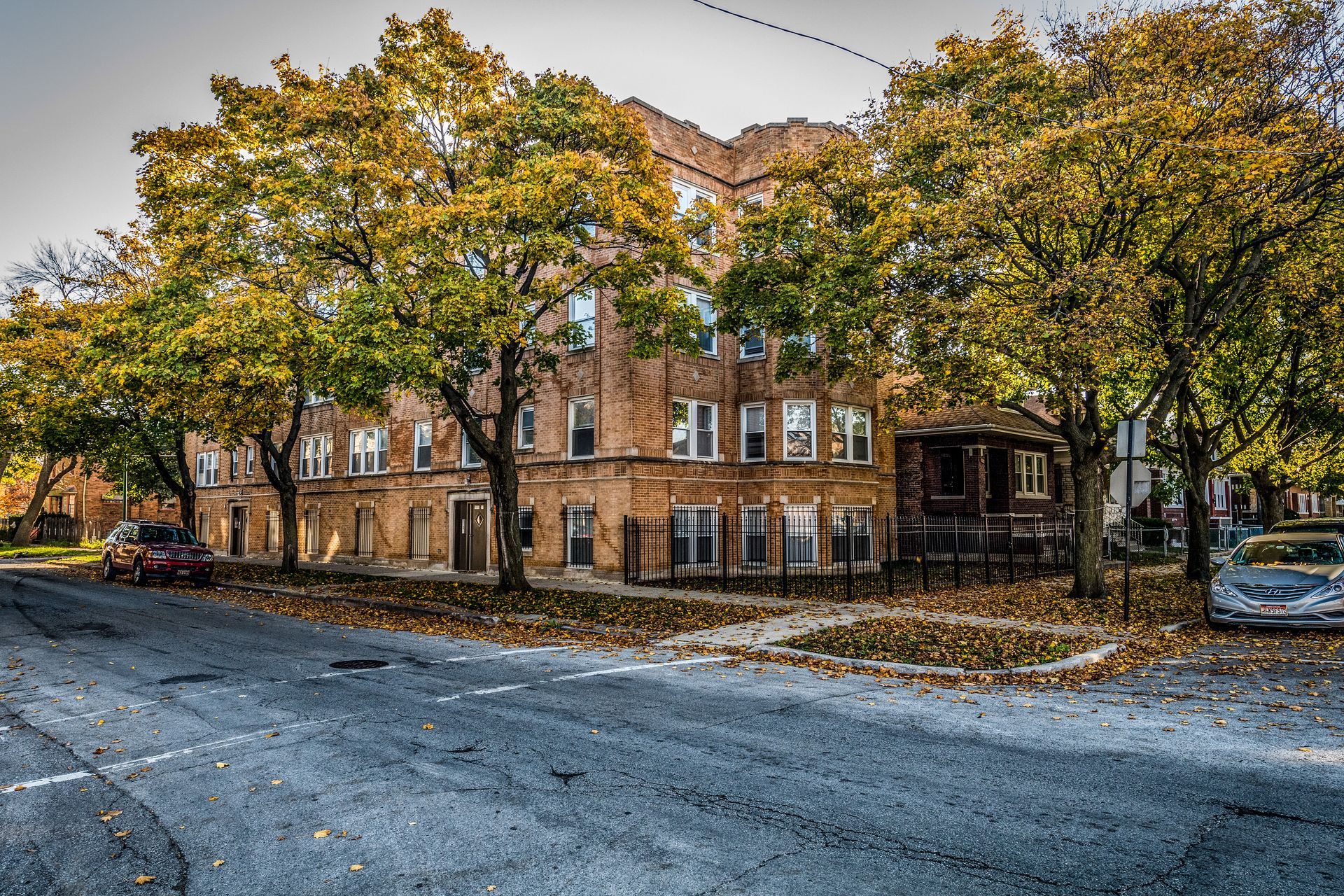 A brick apartment building with fall foliage lining the street in an urban setting.