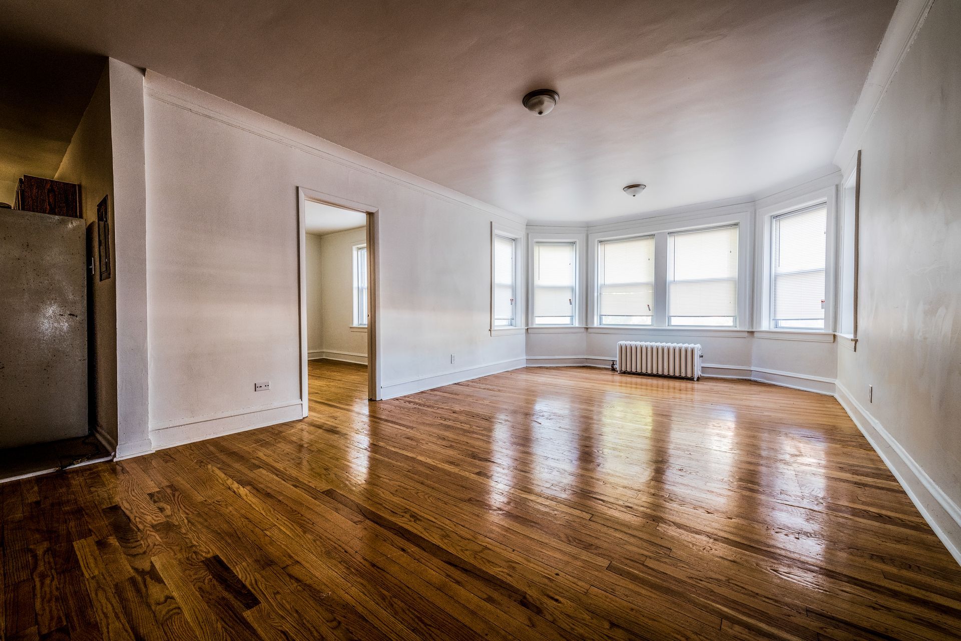 Empty living room with wood floors, white walls, and a bay window.