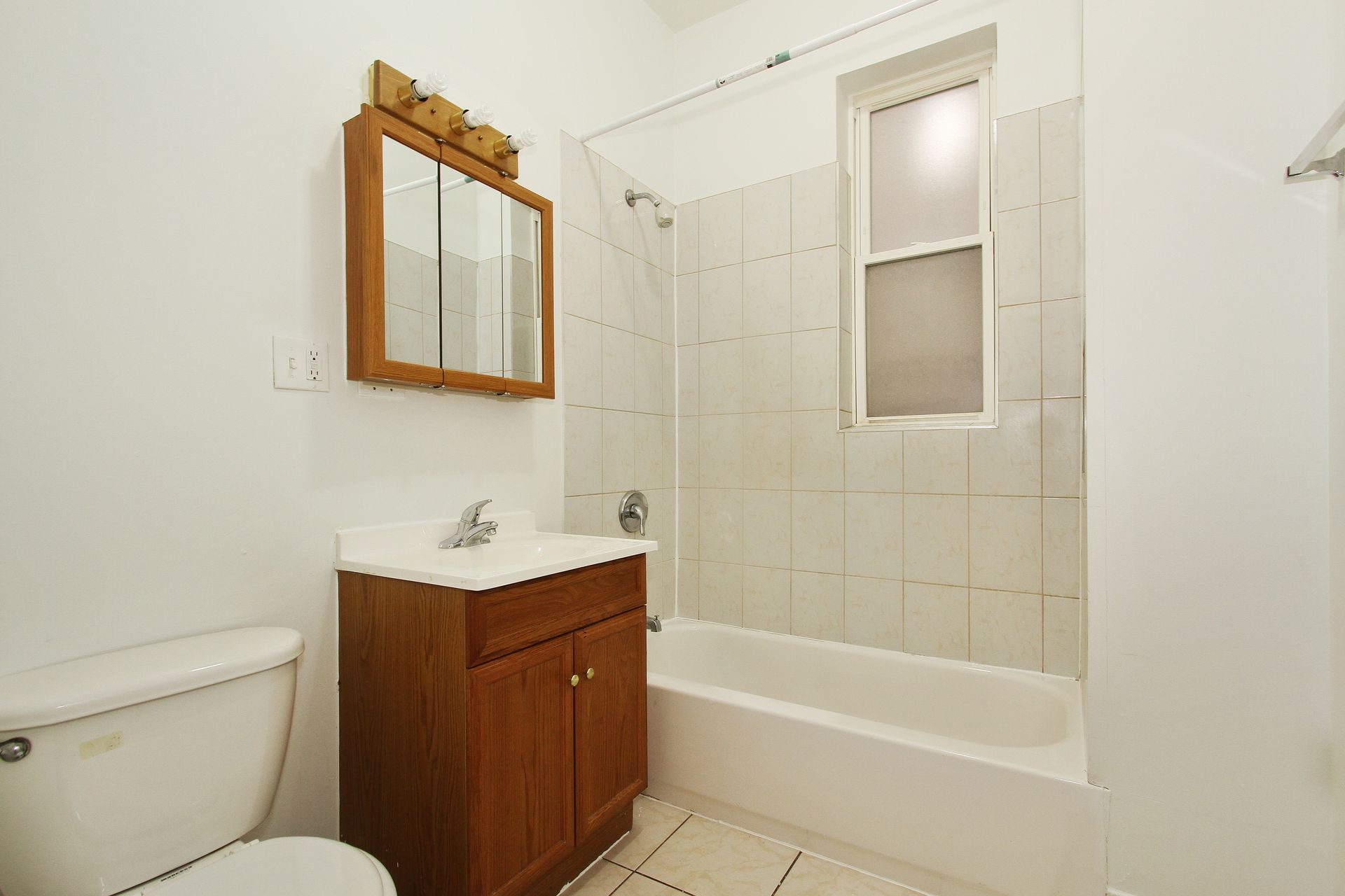 Bathroom with a toilet, vanity, and shower/tub combo. Brown vanity, white walls and tiles.