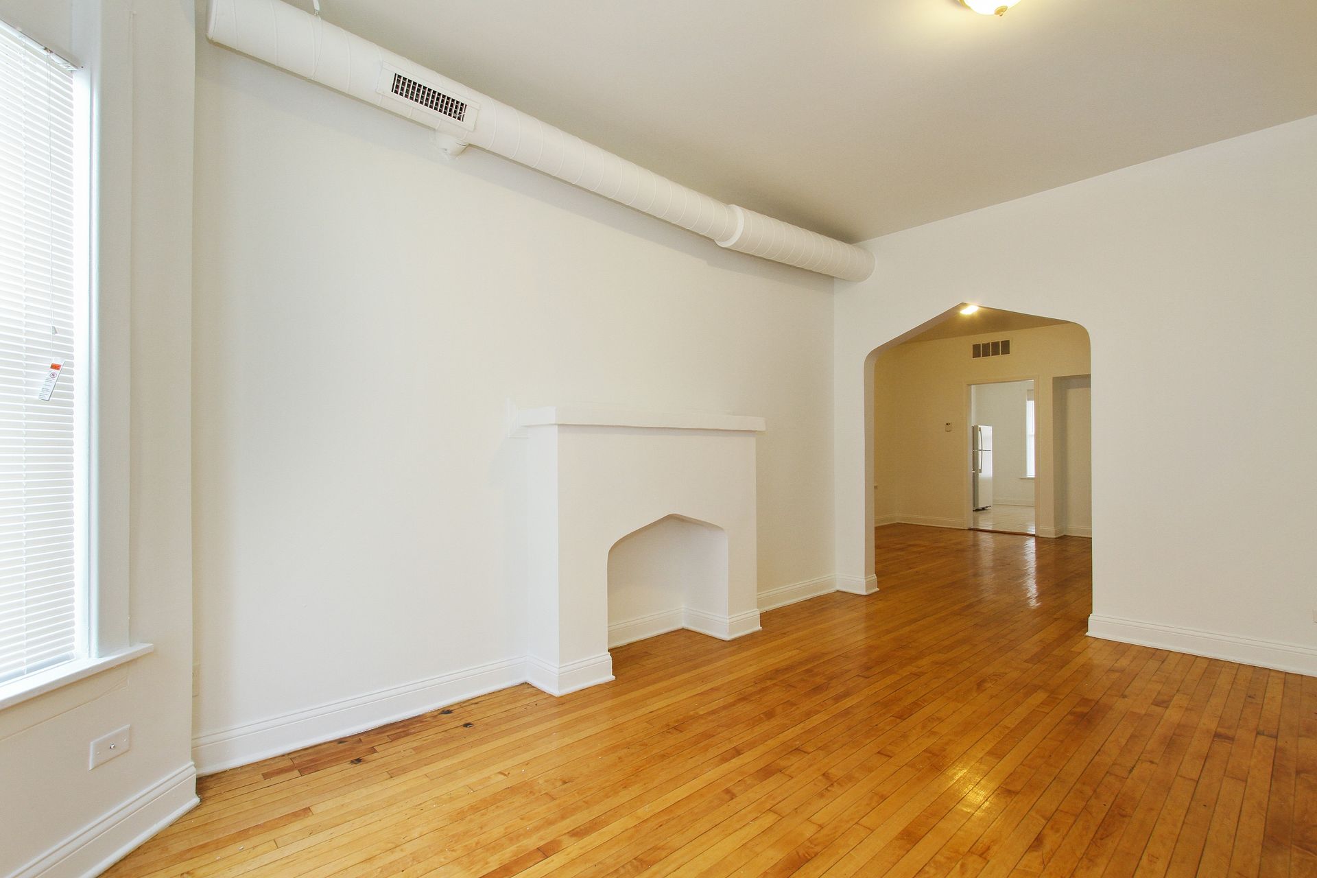 Empty living room with wood floors, white walls, arched doorway, and fireplace.