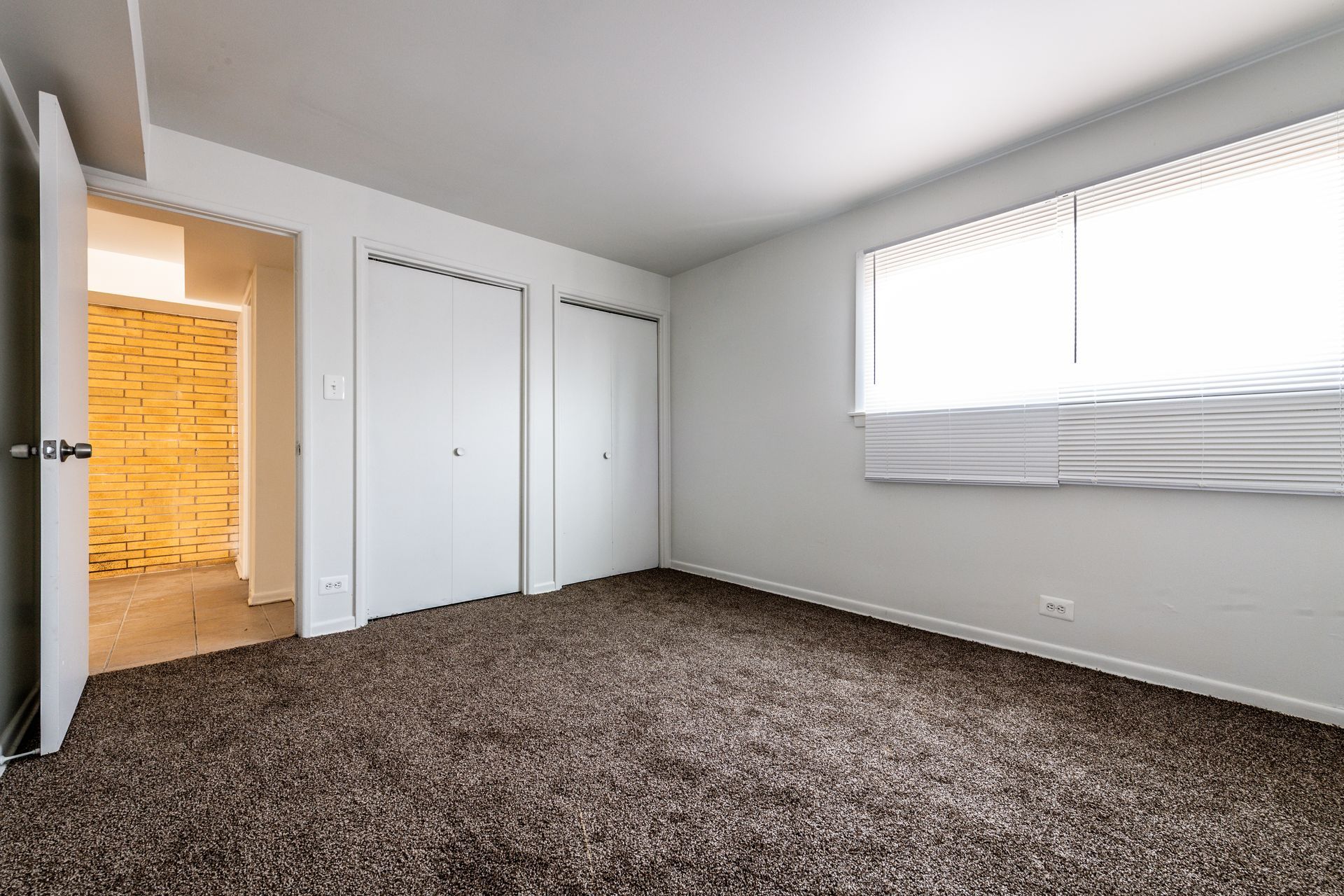 Empty bedroom with brown carpet, two white closets, and a window.