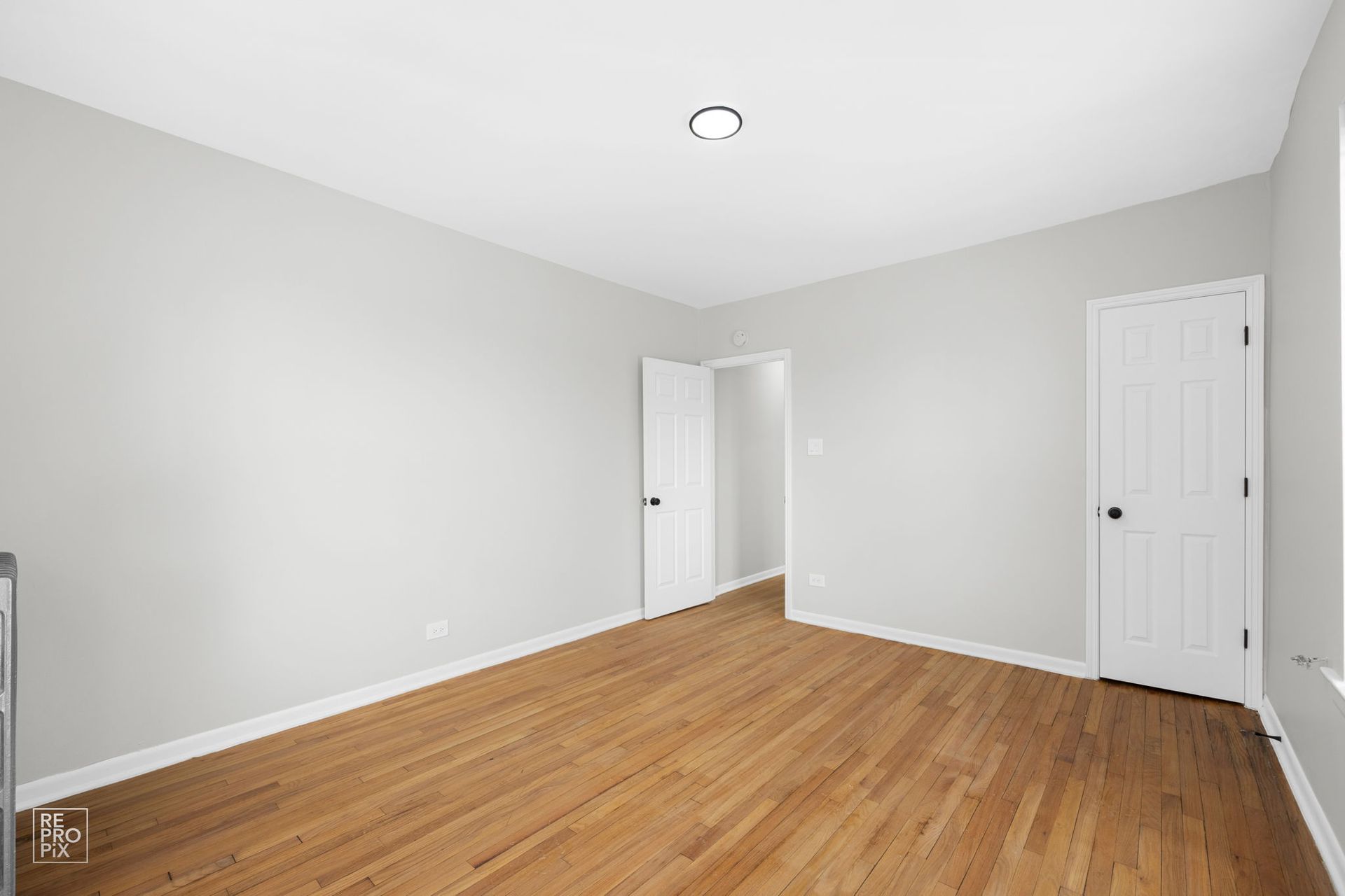 Empty room with hardwood floors, white walls, and two white doors.