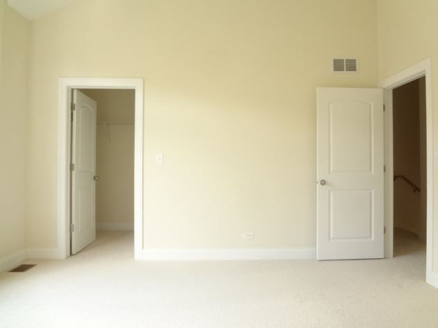 Empty room with three white doors, beige walls, and light carpet.