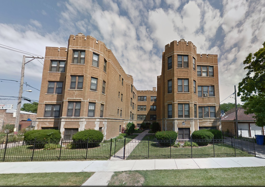 Brick apartment building with decorative turrets and small front yard.