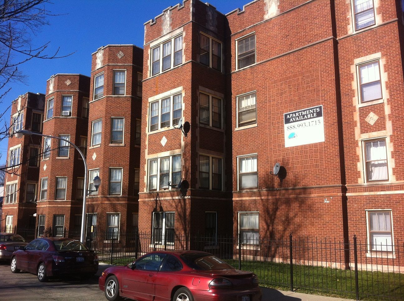Multi-story brick apartment building with cars parked in front.