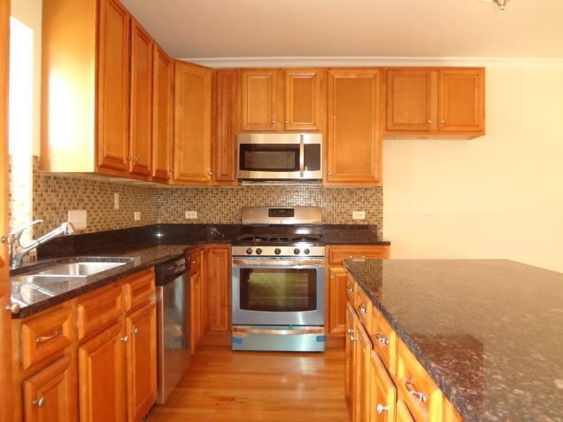 A kitchen with wooden cabinets, stainless steel appliances, and a granite countertop island.
