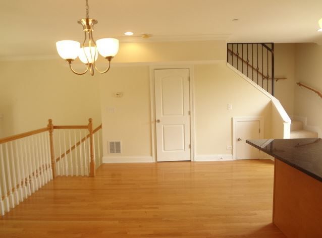 Empty room with hardwood floors, staircase, chandelier, and a white door.