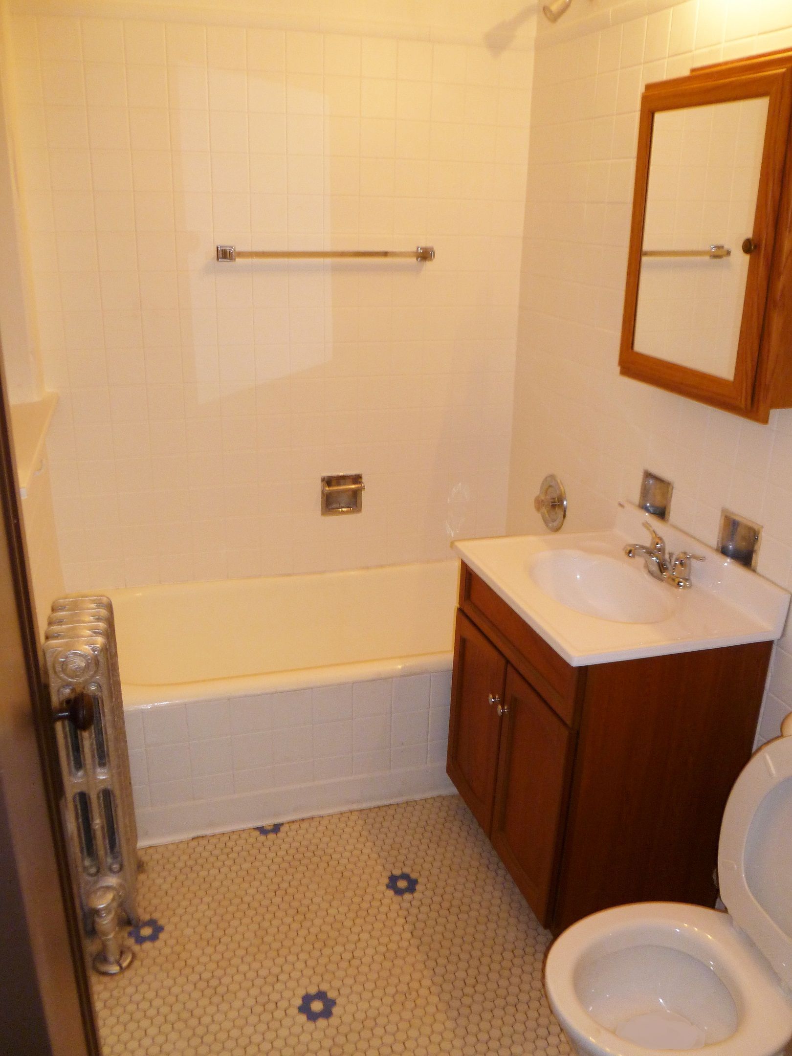 Small bathroom with white tub, sink, toilet, and brown cabinet. White and blue tile floor.