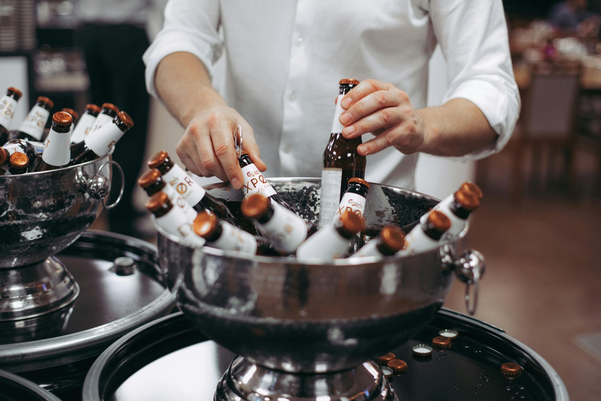 Hands arranging small bottled drinks in metal bowls on a table at an event