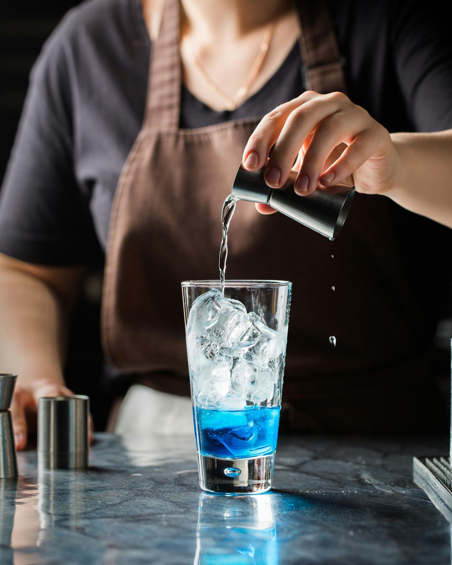 Bartender pouring blue liquid into a glass filled with ice on a bar counter