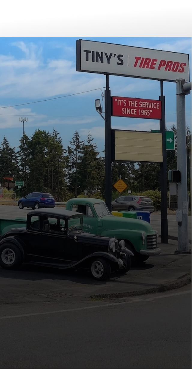 Tiny’s Tire Pro sign above two vintage cars parked outside a tire shop | Tiny's Tire Center
