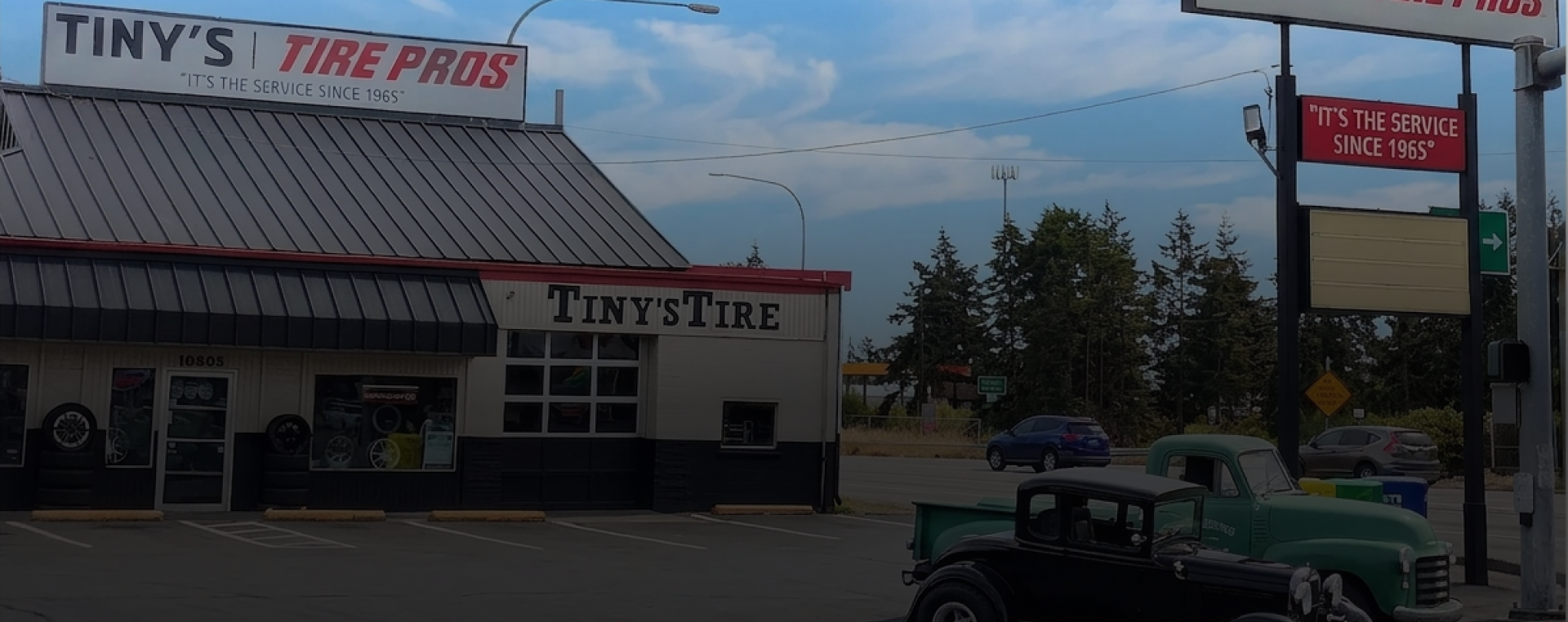 Exterior of Tiny’s Tire Pros auto shop with parking lot and roadside sign at dusk | Tiny's Tire Center