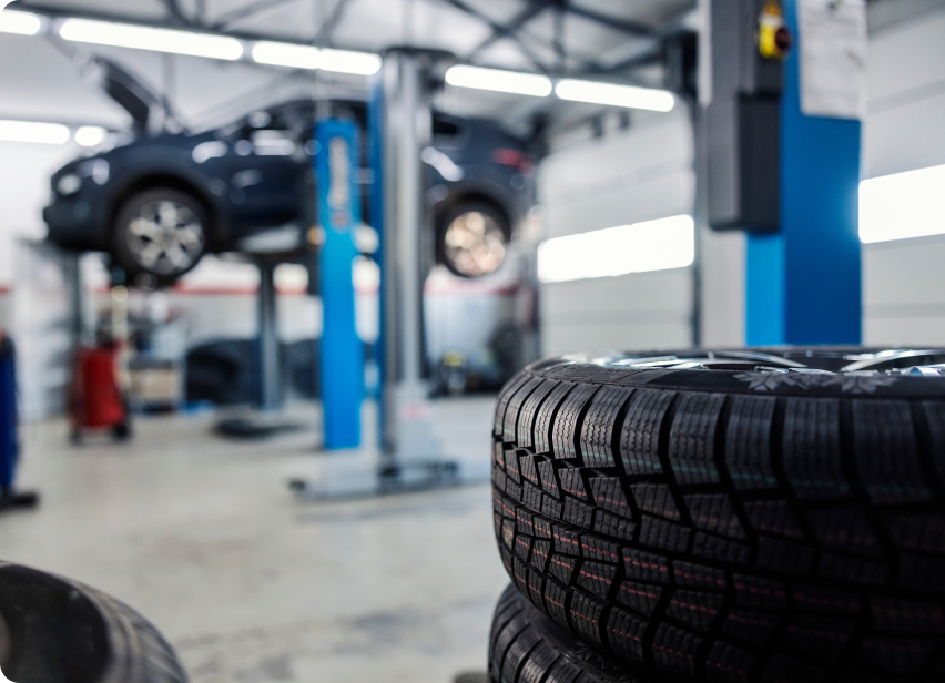 Stack of winter tires in an auto repair shop with a car lifted in the background | Tiny's Tire Center