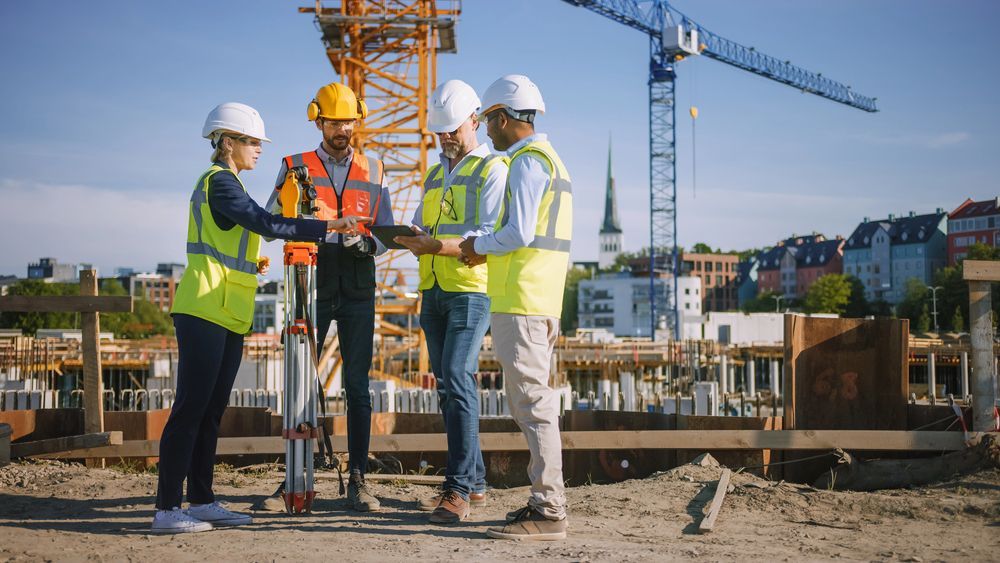 Los trabajadores de la construcción, con cascos y chalecos, se apiñan en una obra en construcción.