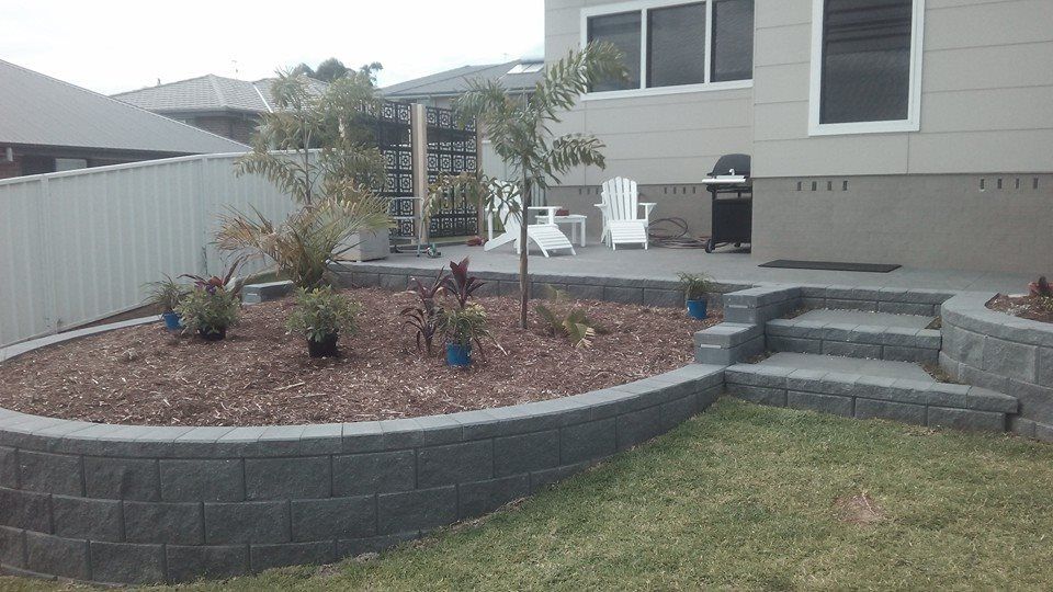 A Backyard With a Brick Wall and Steps Leading to a Patio — Seascapes Landscape Construction in Kendall, NSW