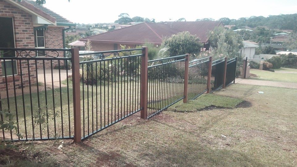 A Metal Fence Surrounds a Grassy Yard in Front of a Brick House — Seascapes Landscape Construction in Kendall, NSW