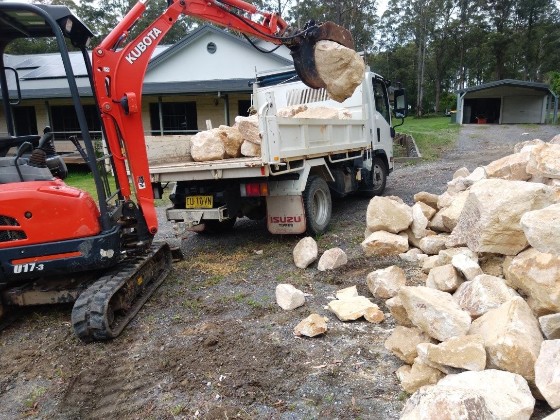 An Excavator is Loading Rocks Into a Dump Truck — Seascapes Landscape Construction in Kendall, NSW