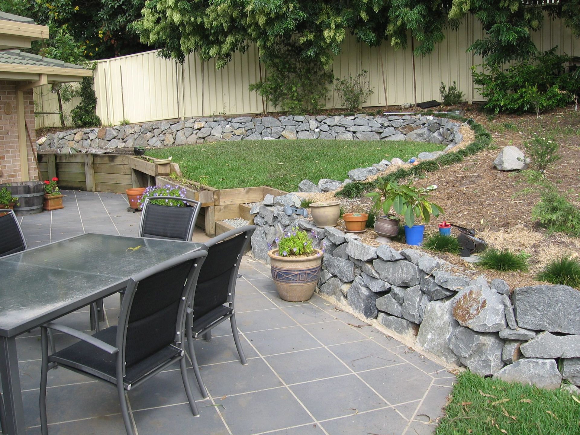 A Patio With a Table and Chairs and Potted Plants — Seascapes Landscape Construction in Kendall, NSW