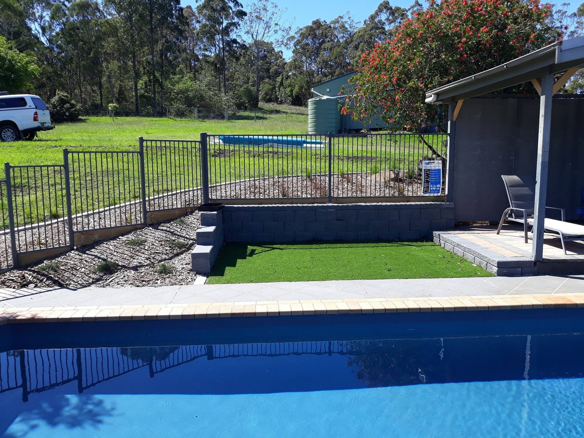 A Large Swimming Pool is Surrounded by a Fence and Grass — Seascapes Landscape Construction in Kendall, NSW