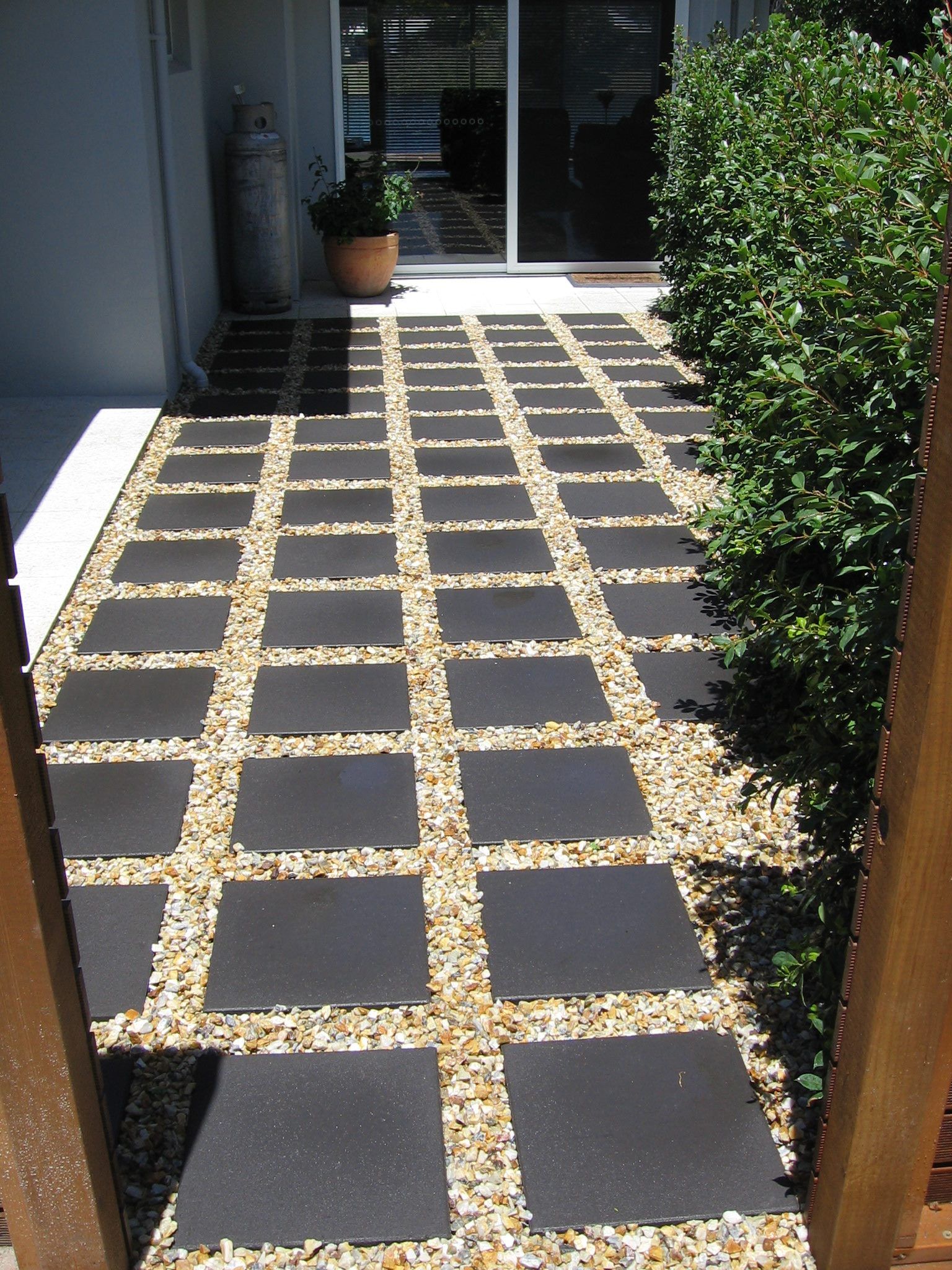 A Walkway With Black Tiles and Gravel Leading to a Sliding Glass Door — Seascapes Landscape Construction in Kendall, NSW