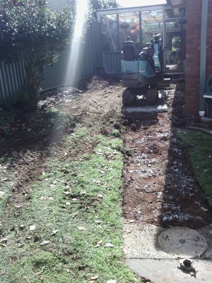 A Small Excavator is Moving Dirt in a Backyard — Seascapes Landscape Construction in Kendall, NSW