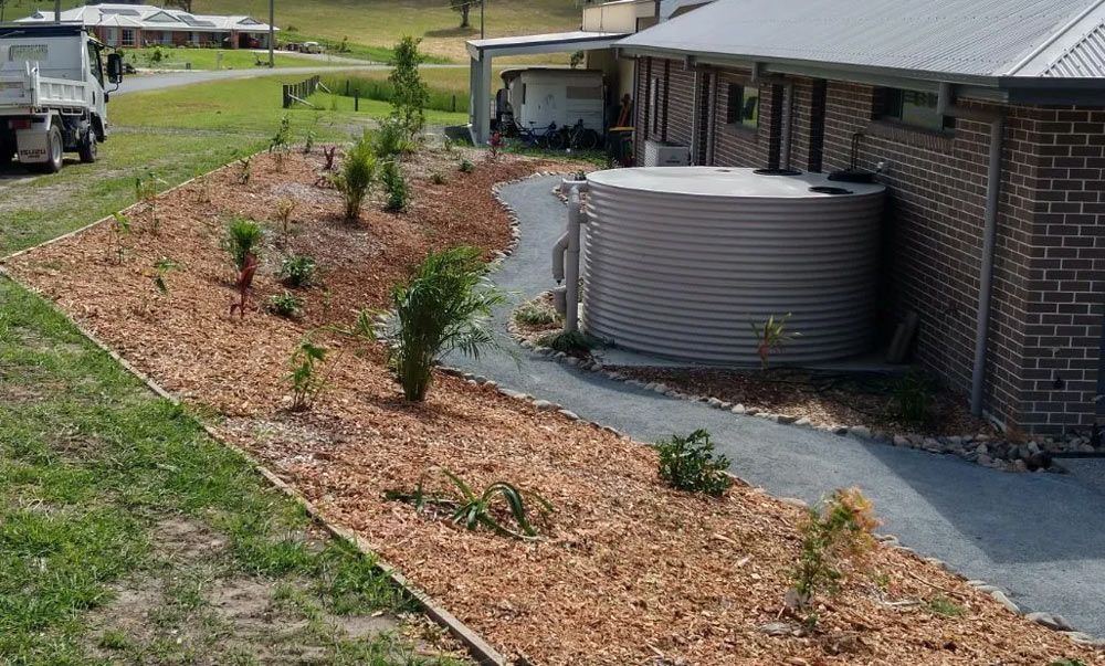 A Brick House With a Water Tank in the Backyard — Seascapes Landscape Construction in Kendall, NSW