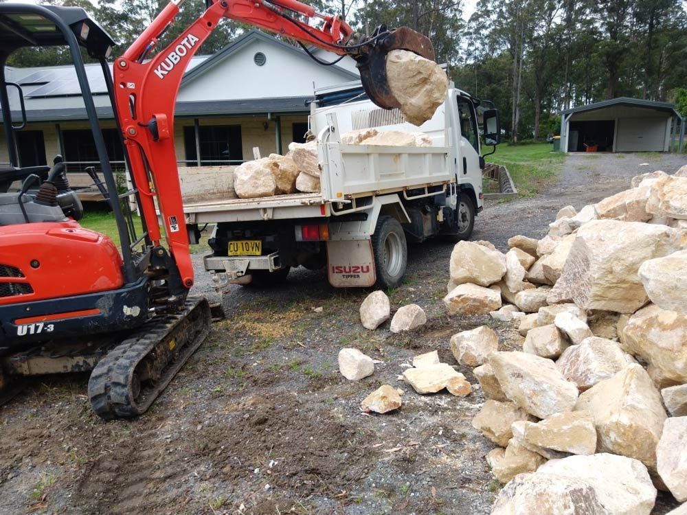 An Excavator is Loading Rocks Into a Dump Truck — Seascapes Landscape Construction in Kendall, NSW