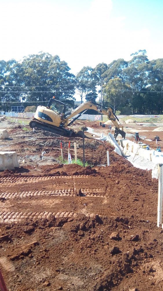 A Small Excavator is Moving Dirt in a Backyard — Seascapes Landscape Construction in Kendall, NSW