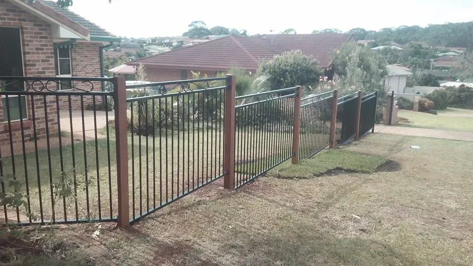 A Metal Fence Surrounds a Lush Green Yard in Front of a Brick House — Seascapes Landscape Construction in Kendall, NSW