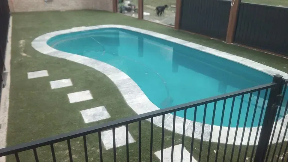 A Large Swimming Pool With a Black Fence Around It — Seascapes Landscape Construction in Kendall, NSW