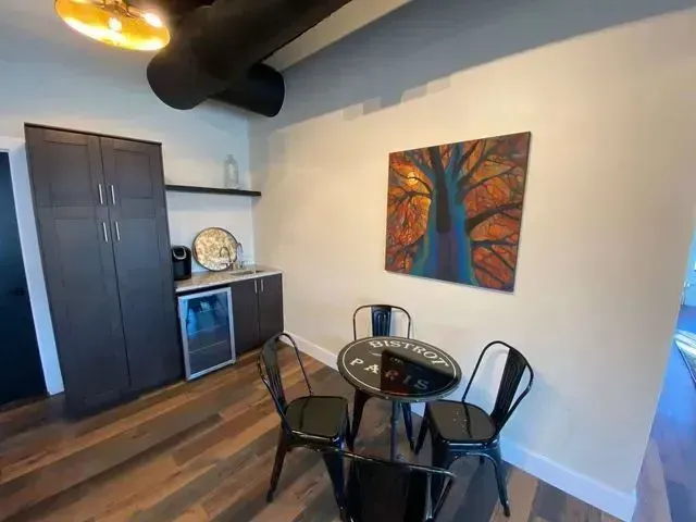 Modern dining nook with black table, metal chairs, cabinet, and abstract wall art