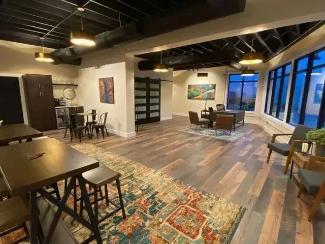 Modern open-plan living room with exposed beams, wood floors, large windows, and a colorful rug