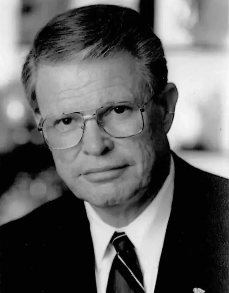 Black-and-white portrait of a man in glasses, suit, and tie, looking at the camera.