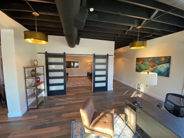 Modern office with wood floors, black ceiling beams, desk, chair, lamp, and sliding doors to a conference area