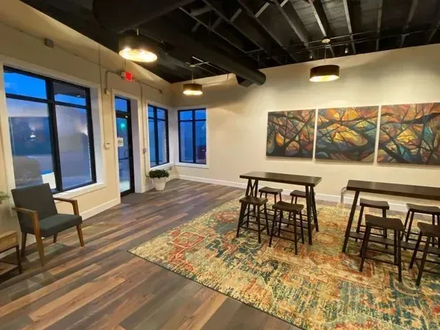 Modern lounge with large windows, chairs, tables, colorful rug, and abstract wall art