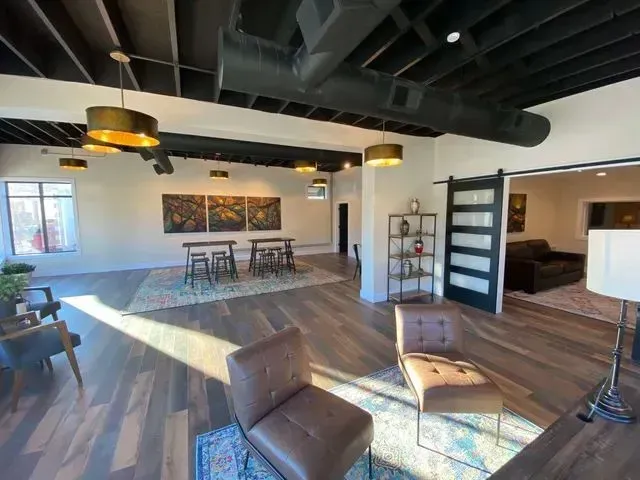 Modern open-concept living room with wood floors, exposed beams, and seating area by large windows