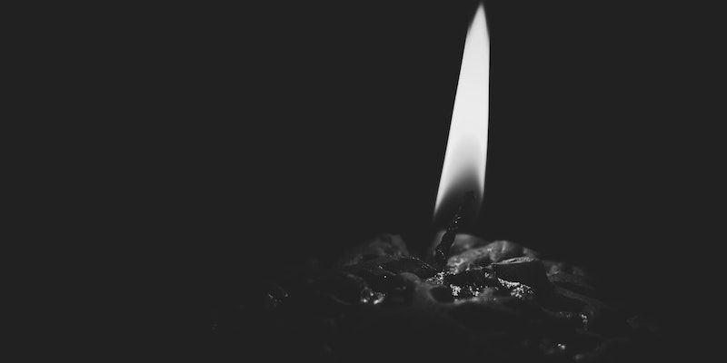 A single lit candle with a bright flame on a dark background