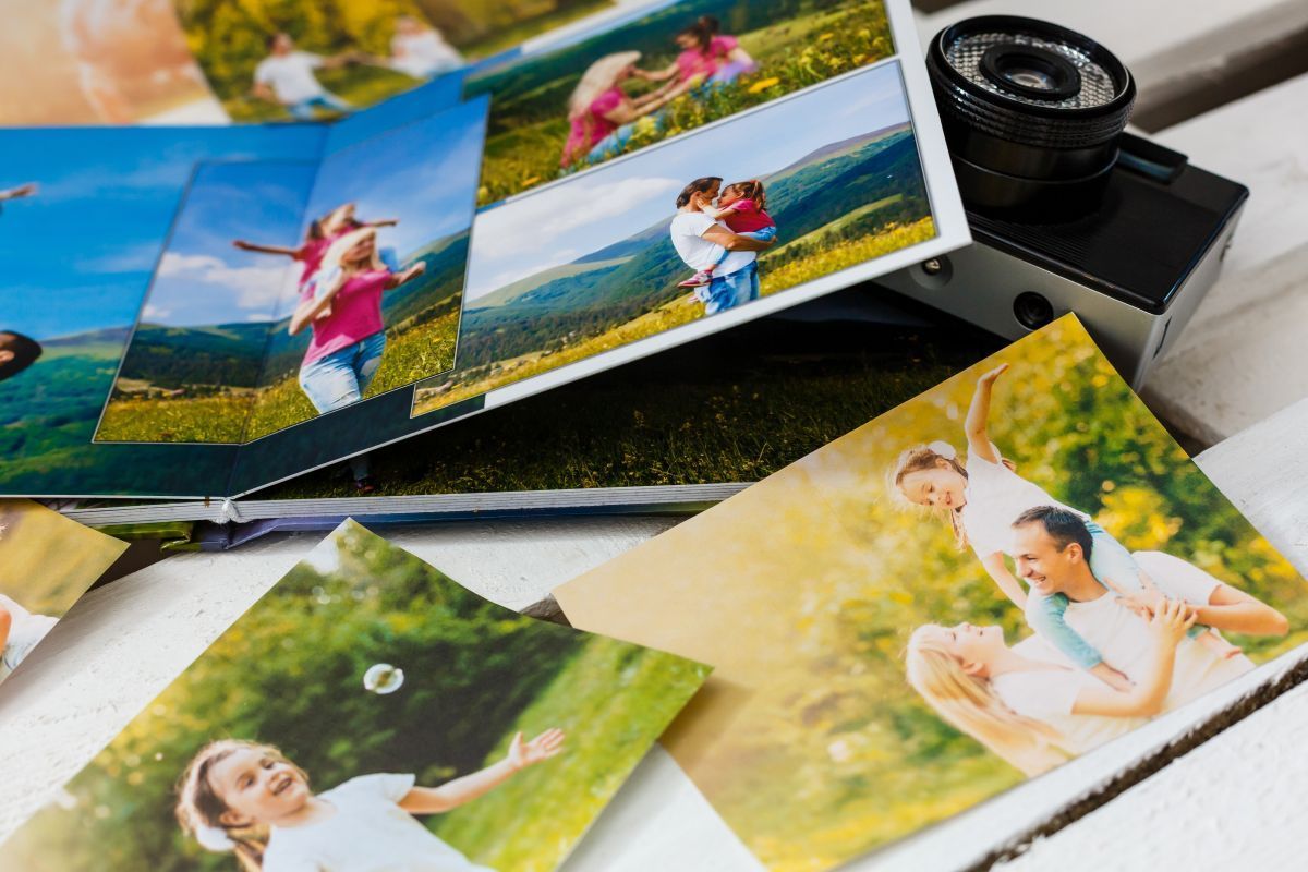 Photo books and prints showing colorful family portraits on a table next to a camera lens