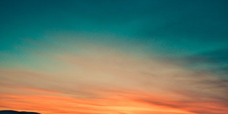 Orange and teal sunset sky with wispy clouds over a dark horizon