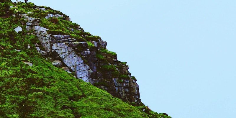 Steep rocky hillside covered in lush green vegetation against a clear blue sky