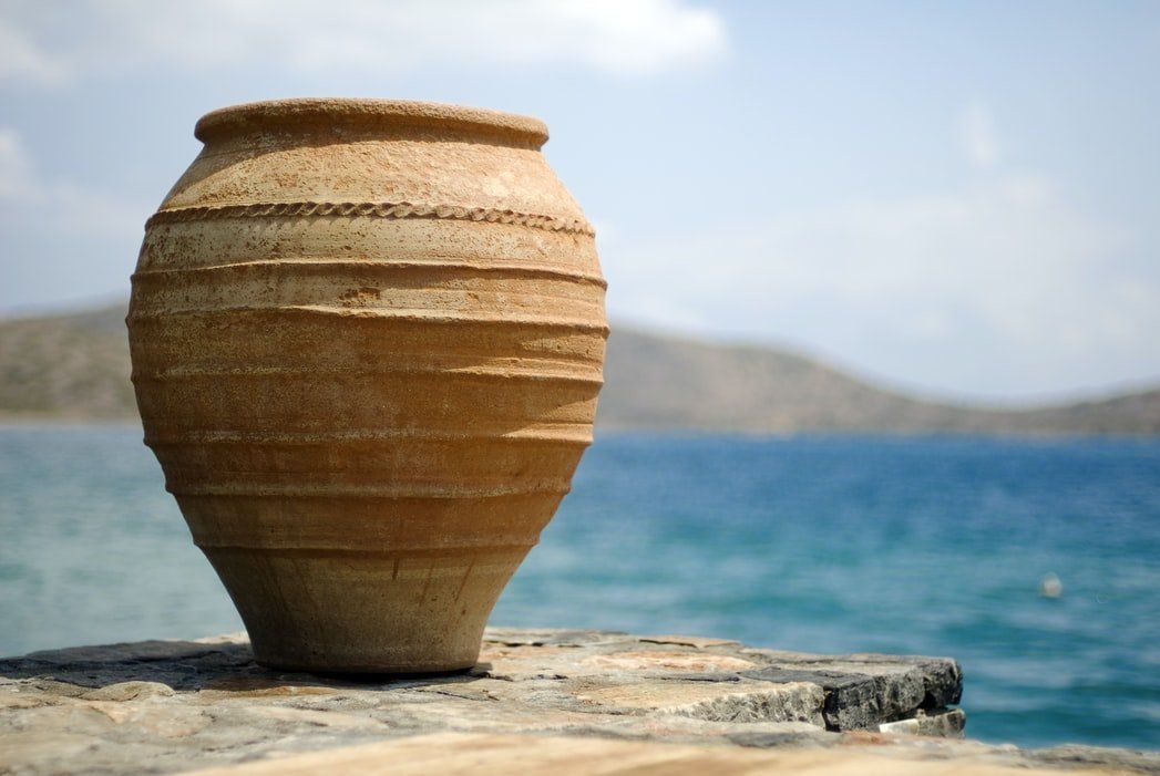 Clay pot on a stone ledge by the sea, with blue water and distant hills in the background
