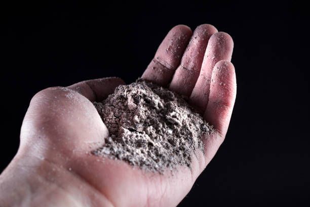 Open palm holding a mound of gray powder against a dark background