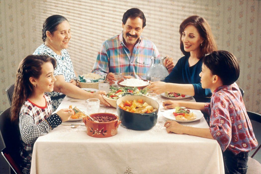 Family gathered around a dining table, sharing a meal and smiling in a warm home setting.