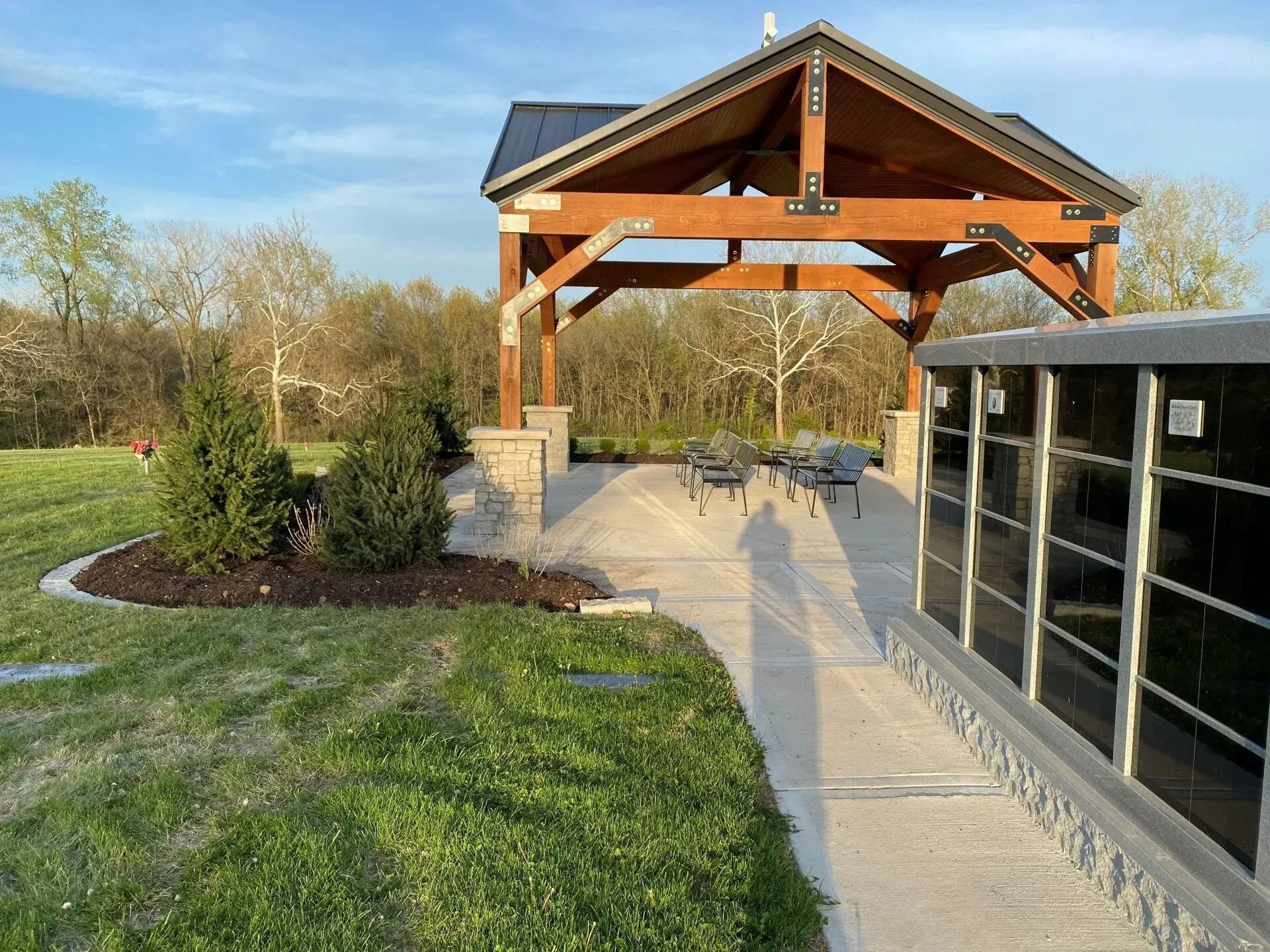 Wooden pavilion beside a concrete walkway and glass wall in a grassy park at sunset