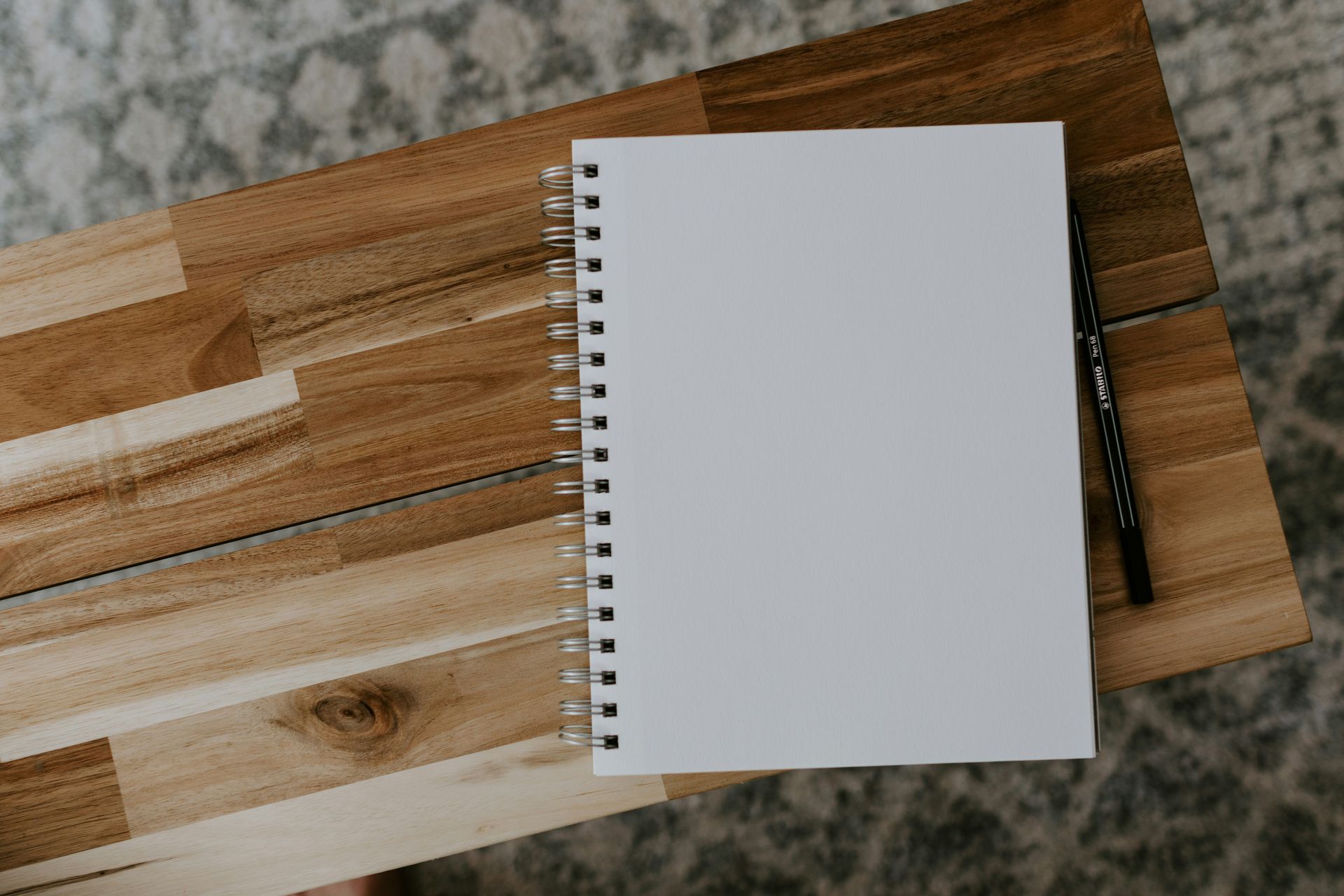 Blank spiral notebook on a wooden table beside a black pen and transparent ruler